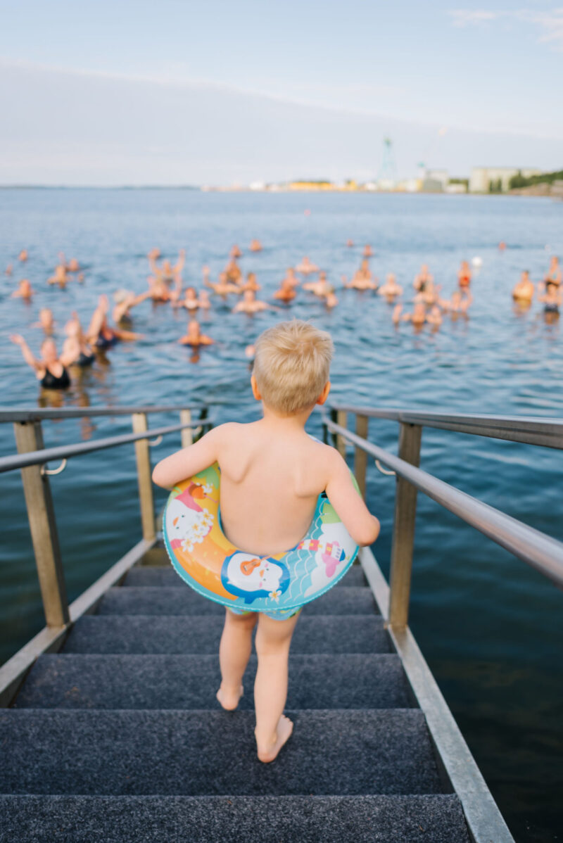 Pieni lapsi menossa uimaan uimarenkaan kanssa mereen jossa on paljon uimareita