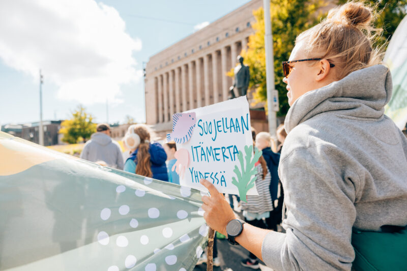 ihmisiä mielenosoituksessa kantamassa kylttiä, jossa lukee Suojellaan Itämerta yhdessä