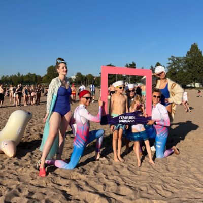 ihmisiä poseeraa hiekkarannalla erilaisissa uima-asuissa