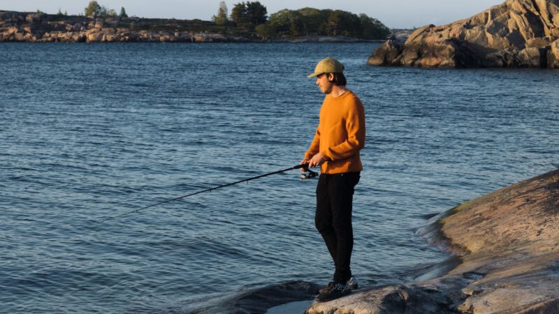 Mies kalastaa rantakalliolla