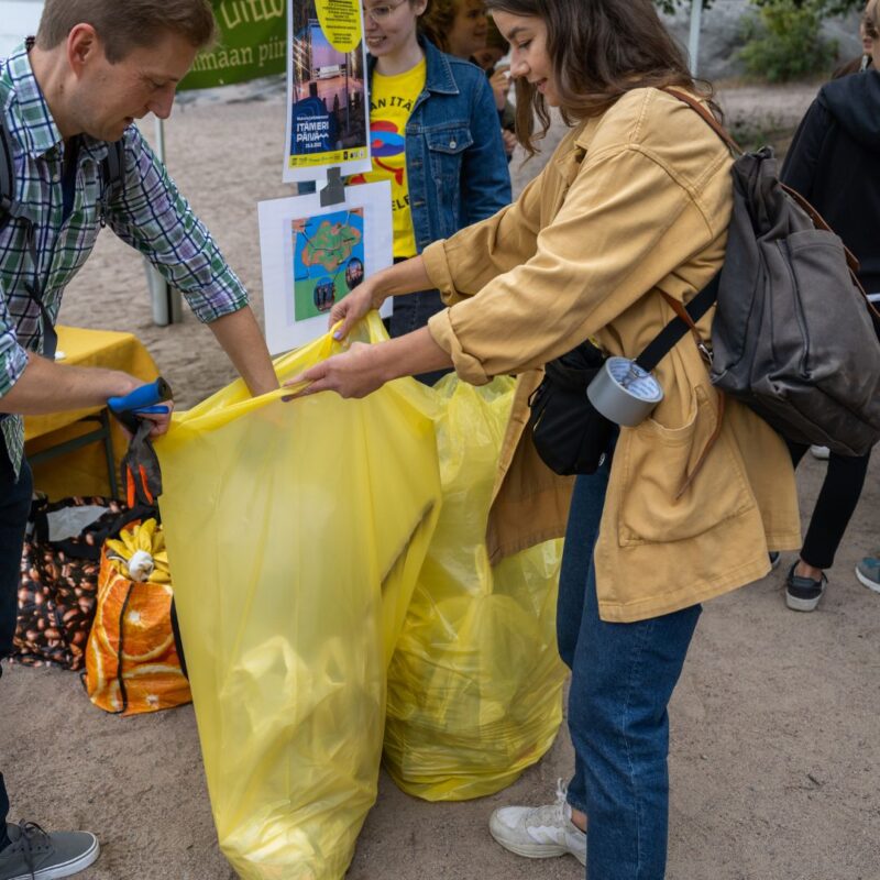 Kaksi ihmistä avaa isoa roskajätesäkkiä