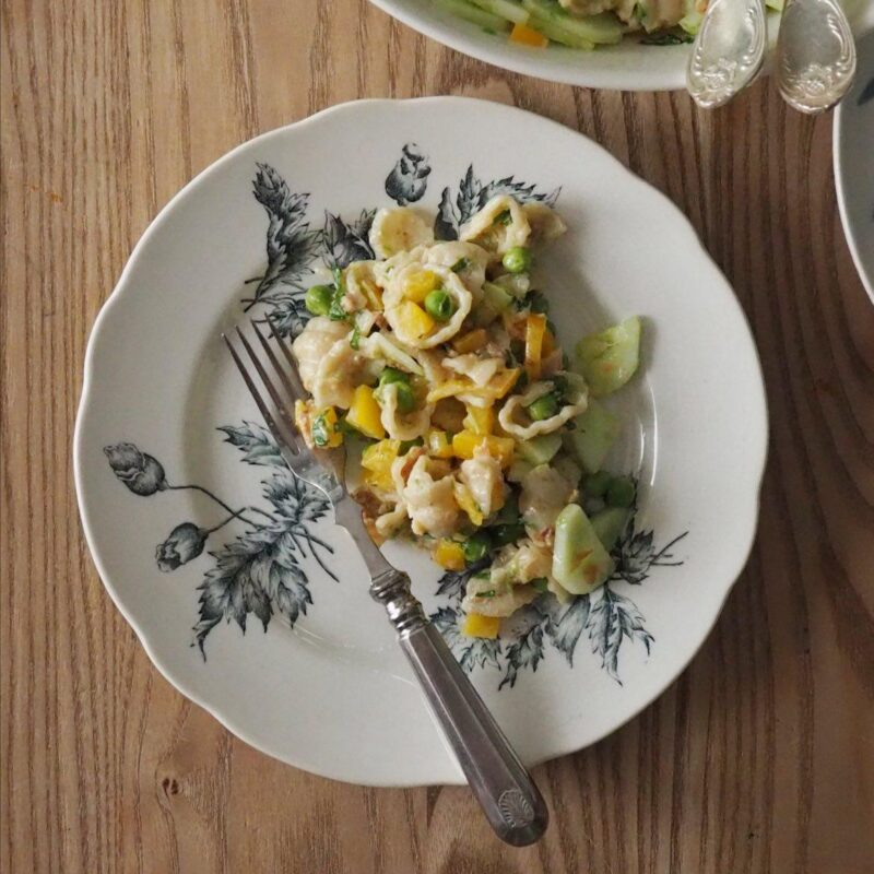 Lautasella kalaa, pastaa, maissia ja kurkkua, vieressä suurempi kulho samaa salaattia, kaikki asetettuna puupöydälle.