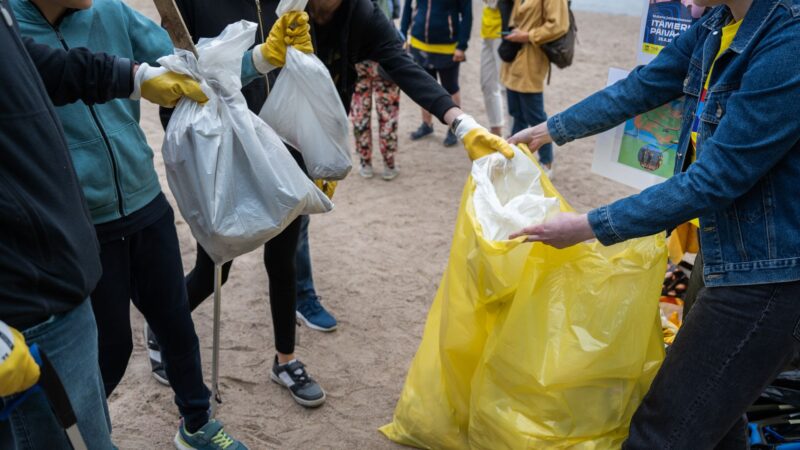 People collecting trash and putting it into large yellow garbage bags outdoors.